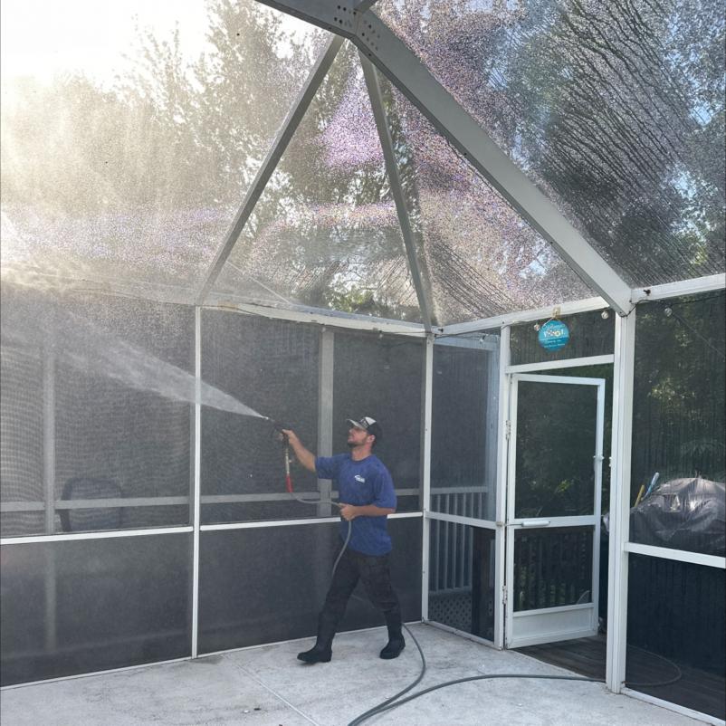 man using a pressure washer to clean a screened enclosure area in a residential backyard
