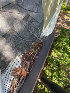 clogged gutter filled with leaves and debris needing cleaning with evidence of nearby foliage and a cleaning tool