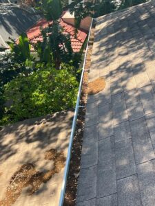 gutter cleaning showing buildup of debris and leaves on roofing surface with clear separation between clean and dirty areas