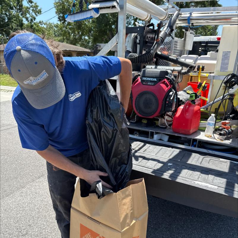 a worker from south tampa gutter and window cleaning placing a black bag into a cardboard box at a job site