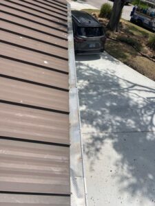 metal roof with gutter system and nearby vehicle parked in driveway shadows from trees are visible on ground