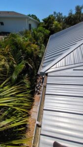 gutter cleaning services being performed on a metal roof with greenery surrounding the area and clear blue sky