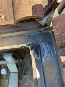 gutter repair with sealant applied along joints under roof tiles with visible debris in the surrounding area