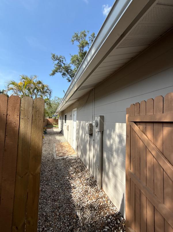 cleaning services performed on a residential building exterior with access from a gated side yard and gravel pathway