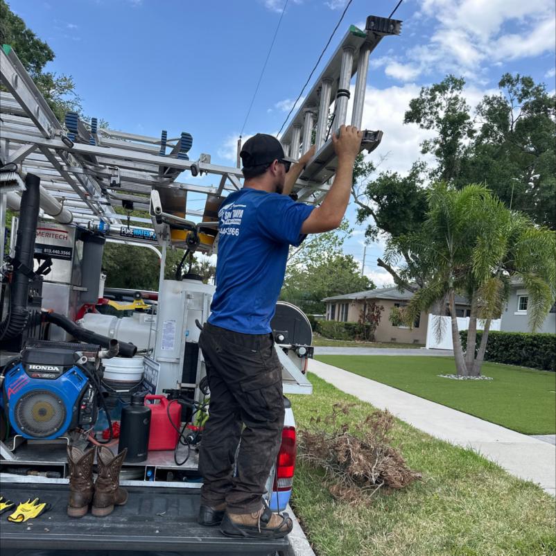 a worker lifting a ladder from the back of a truck with cleaning equipment visible lawn and trees in the background
