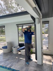 technician inspecting or repairing a screen enclosure near a pool area in a residential setting