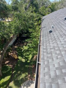 gutter cleaning and maintenance on a residential roof surrounded by trees and a well-kept lawn