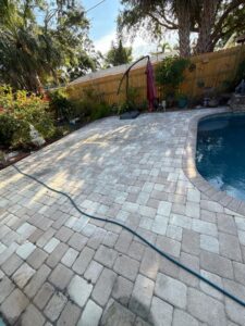 patio cleaning service in residential yard with brick pavers near a pool and hose in view