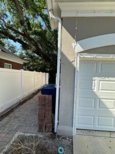 gutter installation and maintenance along the side of a house next to a brick column and a blue trash bin