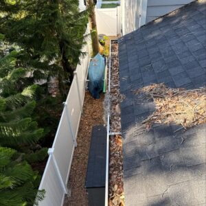 gutter cleaning service with debris and leaves accumulated along the edge of the roof near a fence and vegetation