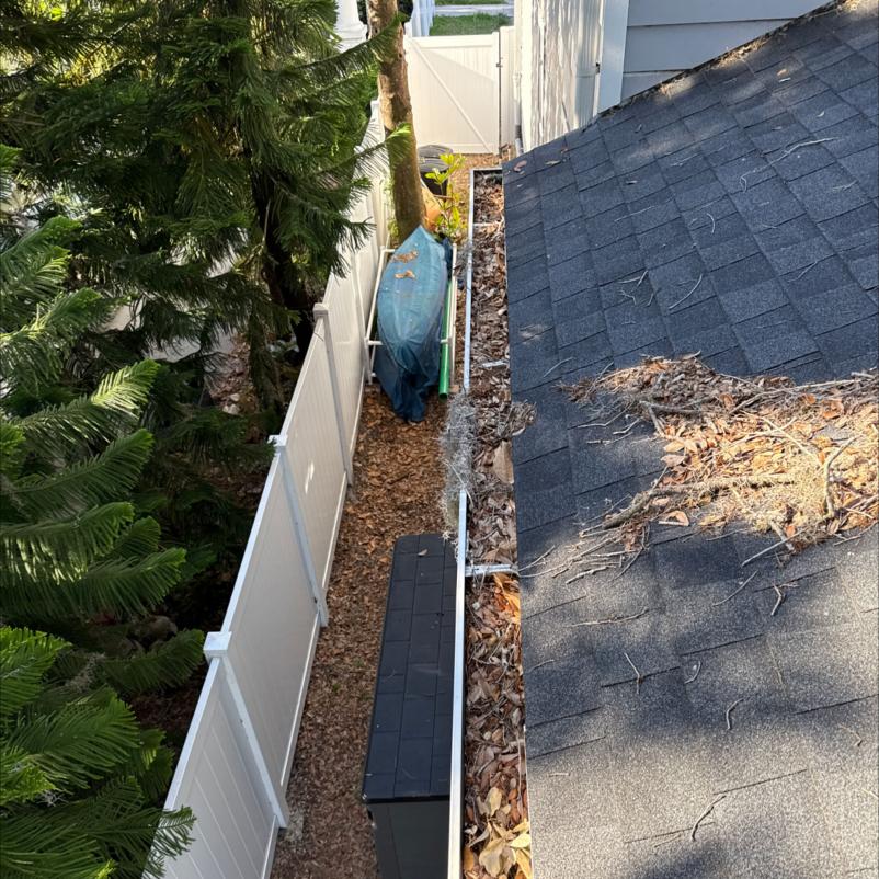 gutter cleaning service with debris and leaves accumulated along the edge of the roof near a fence and vegetation
