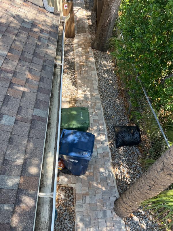 a view of a roof edge with a gutter next to a stone walkway and trash bins placed beside it