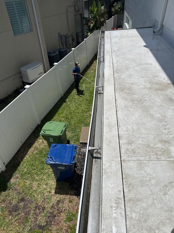 gutter cleaning with equipment in a residential area green and blue trash bins in view grass area alongside a fence