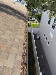gutter cleaning service removing leaves and debris from a roof edge showing significant buildup and blockage