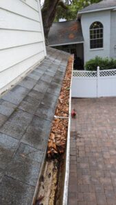 gutter cleaning service removing leaves and debris from gutters on a sloped roof near a brick patio and home