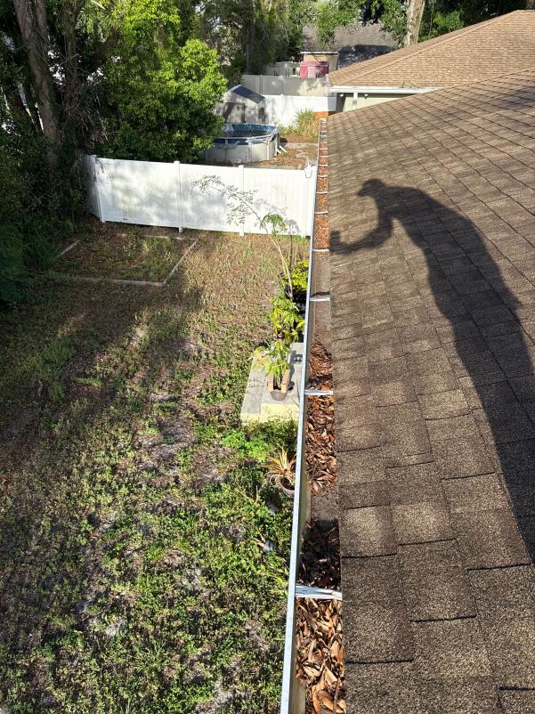 gutter cleaning service with leaves and debris visible on a roof edge and a shadow of the worker