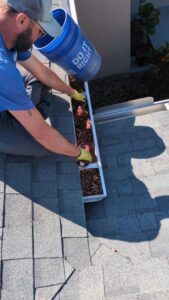 gutter cleaning by removing leaves and debris from a rooftop gutter using a bucket and gloves