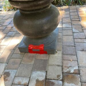 a stone pedestal wrapped in red tape sitting on patterned pavers with some water stains visible nearby