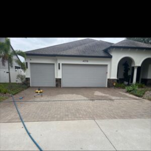 paver cleaning being done on a driveway with a flat surface cleaner and a hose nearby