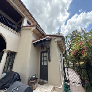 gutter cleaning and window washing on a light colored house with a tiled roof and lush landscaping nearby