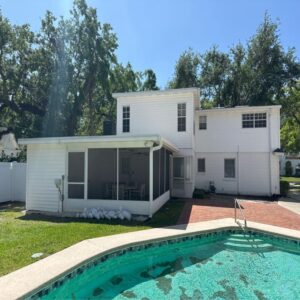 two story white house with a screened porch and a swimming pool surrounded by green grass and trees
