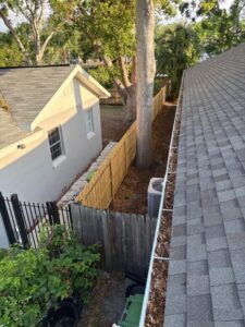 gutter cleaning showing debris along the edge of a roof with visible trees and a wooden fence in the background