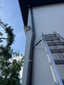 cleaning gutters using a ladder with a clear blue sky and greenery in the background