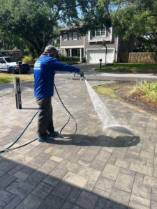 man using a pressure washer on a brick paved surface removing dirt and grime from the patio area
