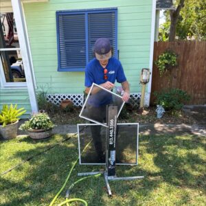 a technician cleaning window screens outside a house using a stand and hose for water supply