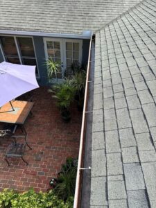 roof maintenance with a clear view of gutters and patio furniture surrounded by plants and brick pavement