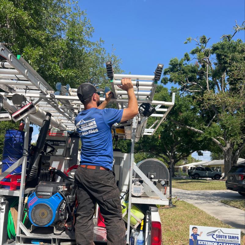 a worker organizing equipment on a truck preparing for window cleaning and gutter services in a residential area