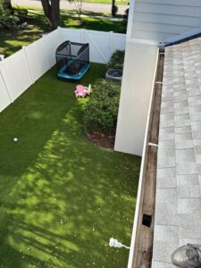 gutter cleaning showing leaf buildup on a roof with artificial grass and a trampoline in the yard below