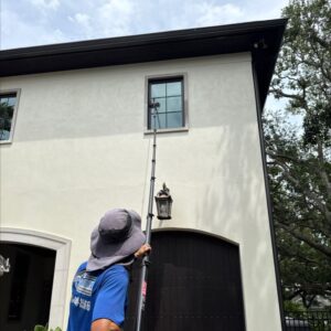employee using a long pole to clean a second story window on a house with a light fixture nearby
