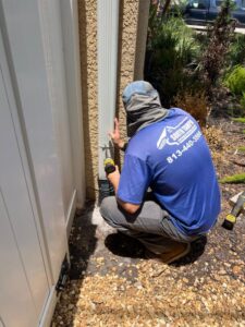 worker securing a downspout using a power drill in a landscaped area with gravel and plants around
