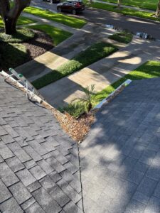 cleaning debris from roof valleys with a ladder placed on the roof and landscaped area below