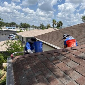 workers cleaning gutters on a sloped roof wearing hats and using buckets for debris collection