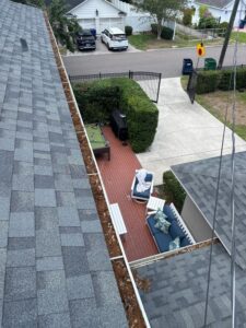 gutter cleaning service showing debris accumulation on roof and gutters with a view of patio furniture below
