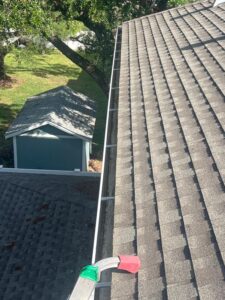 gutter cleaning in progress with ladder and vacuum equipment near a roof and trees in the background