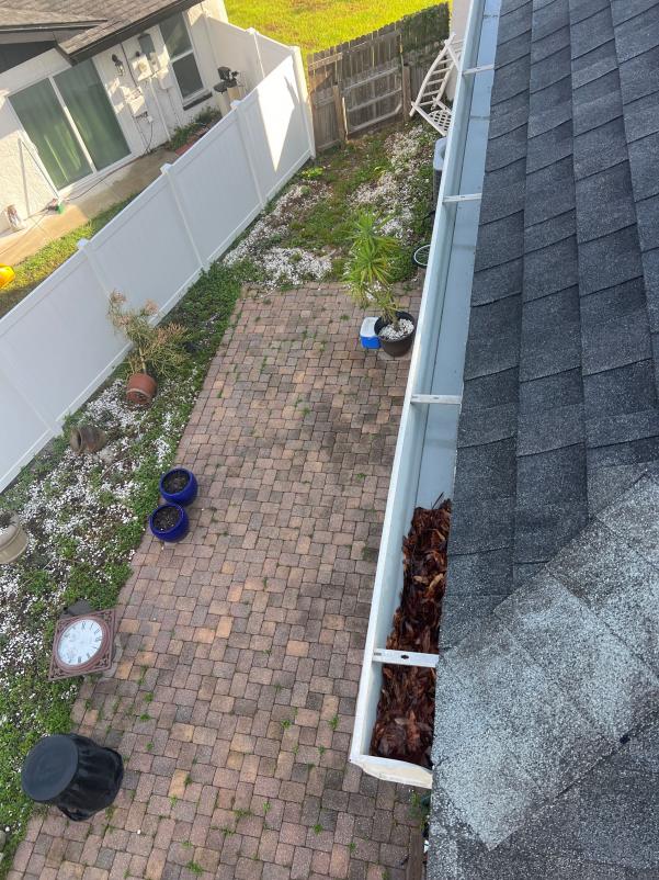 gutter cleaning service showing debris in the gutter and a view of a landscaped yard with pavers and plants