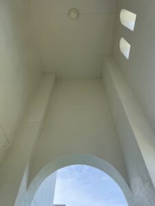 clean white ceiling with light fixture and arched opening showing blue sky above