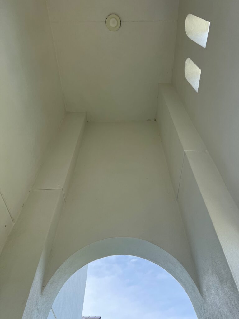 clean white ceiling with light fixture and arched opening showing blue sky above
