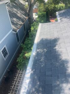 gutter cleaning along a roof edge with green shrubs and landscaping visible in the surrounding area