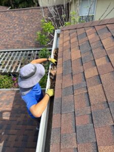 gutter cleaning service removing debris and leaves from gutters wearing yellow gloves on a sloped roof