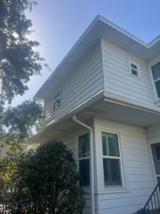 south tampa gutter and window cleaning inspecting and cleaning a home's white vinyl siding with overhanging roof and greenery around