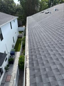 cleaning of a gray shingle roof with visible gutters and neighboring houses in the background showcasing residential landscape