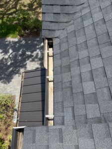 gutter cleaning service showing debris accumulation in a gutter near a roof edge with shingles and surrounding landscaping