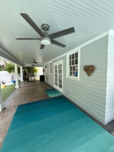 cleaning an outdoor patio area featuring a light gray wall and large ceiling fans with turquoise mats on the ground