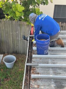 cleaning gutters by removing debris from a rooftop with a blue bucket on the side and a tool in use