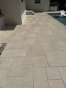 cleaning a light colored patio surface near a swimming pool with a clear view of the house and landscaping
