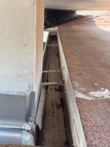 gutter cleaning service showing debris buildup in the gutter near a roof edge with visible mounting hardware